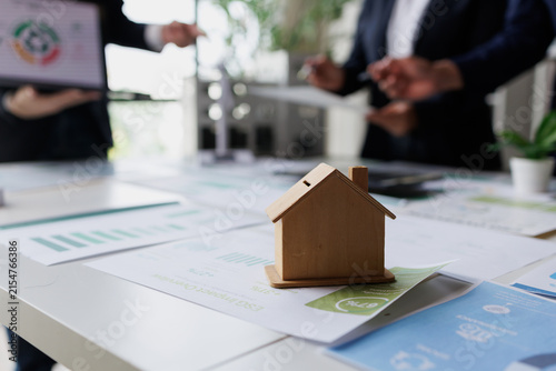 Wooden house model on a table with business people discussing sustainable real estate investment and financial growth