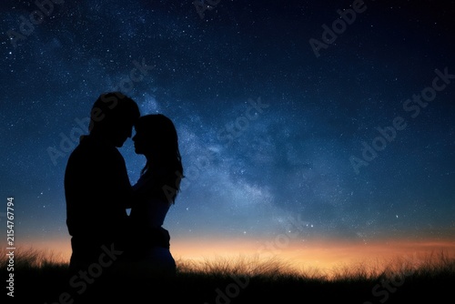 Silhouetted lovers embrace beneath a starry night sky