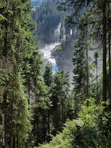 waterfall cascading through a dense alpine conifer forest in a dramatic mountain landscape