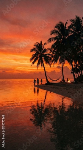 Vibrant sunset over calm tropical water, dramatic orange and red hues reflecting on smooth surface, perfect for serene background visuals or travel stories
