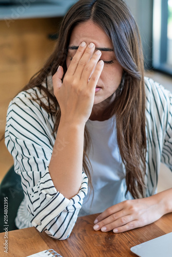 Obraz na płótnie Young woman sitting at desk with hand on forehead, stressed and tired while work