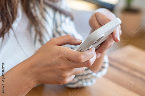 Canvas Print Young woman using smartphone at a wooden table, hands tapping screen while texti