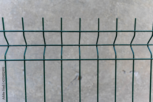 Green, bordered wire fence against crumbling , grey, aged wall .