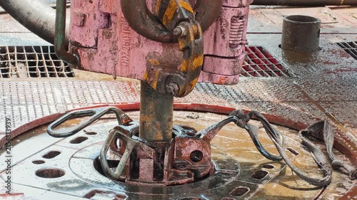 An oilfield worker is setting drillpipe slip equipment and handling drill pipes on a rig floor during exploration. Heavy industrial working scene, close-up.