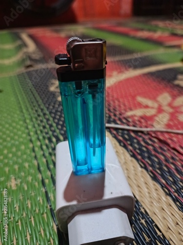Foto Foto menampilkan sebuah korek gas transparan berwarna biru yang berdiri di atas adaptor charger berwarna putih