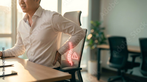 Man suffering from back pain, sciatica, or spinal disc issue while sitting at office desk, glowing red visualization highlights discomfort
