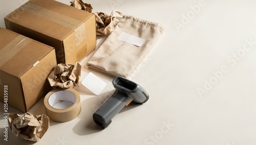 Two cardboard boxes tape dispenser crumpled paper barcode scanner and a drawstring bag on a light surface