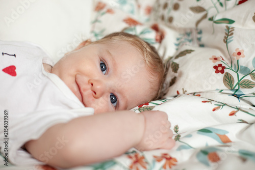 A blue-eyed baby smiles up from a floral bedspread