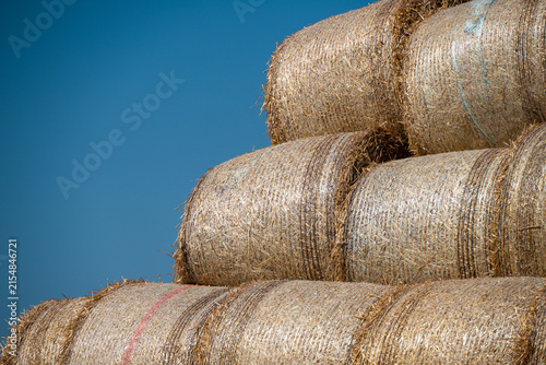 Foto a neat stack of tightly bound, golden round hay bales set against a vibrant, clear blue sky