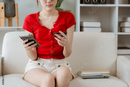 Canvastavla Online Shopping Addiction: A young woman sits on a sofa, engrossed in her smartphone and credit card, highlighting the allure and potential pitfalls of online retail therapy