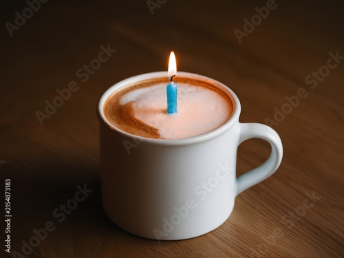 White coffee mug with birthday candle on wooden table for celebration concept