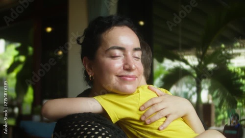 Warm emotional moment of a mother embracing her young child at home, expressing love, tenderness and family affection. Soft daylight and greenery create a peaceful atmosphere.