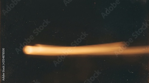 High-speed photograph capturing a luminous projectile in motion against a dark, featureless background, creating a streaking light effect.