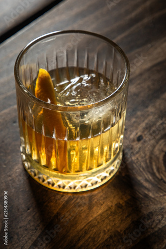 Close up of a classic old fashioned cocktail on a dark wooden background garnished with an orange twist.