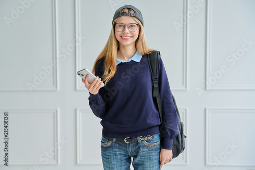 Smiling teenage student with backpack holding phone