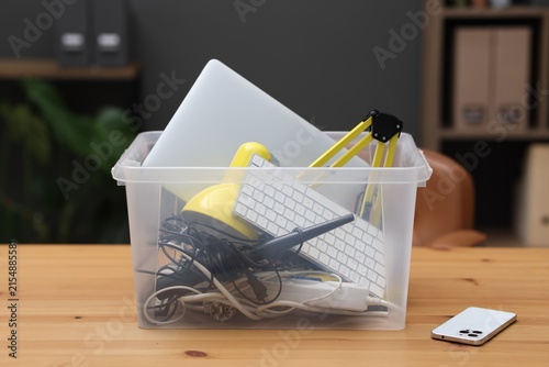 Recycling. Plastic container with different broken household appliances on wooden table indoors