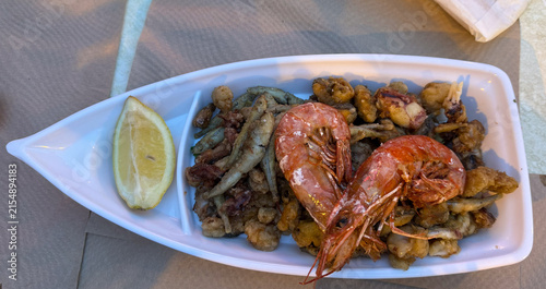 seafood platter arranged on a ceramic plate with a textured tablecloth and napkin, fresh and appetizing top-down view in a restaurant setting with white and brown tones.