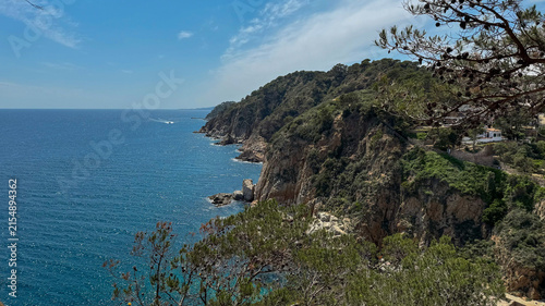 serene aerial view of the mediterranean sea with rocky cliffs and lush vegetation, showcasing the natural beauty of the coastline with vibrant blue and green waters and white clouds.