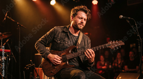 Musician playing electric guitar on stage with audience in background