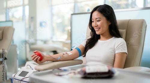 A happy young Asian woman donating blood in a bright medical clinic.
