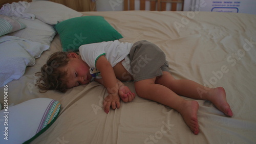фотографія Tired toddler sleeps curled on a large bedroom bed at home, embracing peaceful r