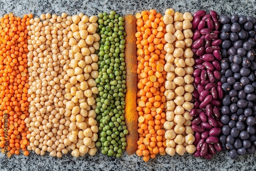 Colorful assortment of legumes and pulses arranged in neat rows on granite surface highlighting variety and healthy vegan food choices