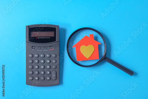 A paper house with golden heart symbol on magnifying glass.