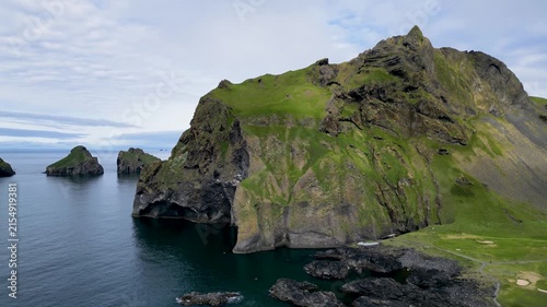 Aerial drone view of Elephant Rock and Heimaklettur mountain under cloudy sky during summer in Heimaey, Vestmannaeyjar, Iceland