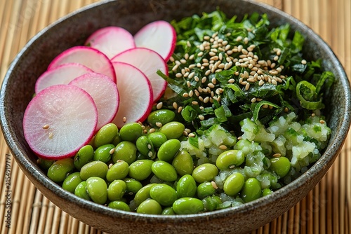 Healthy vegan buddha bowl with radish, edamame, rice, greens, and sesame seeds in ceramic dish on bamboo mat