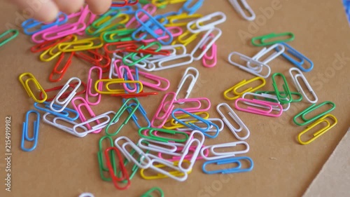 Child's hand touching and sorting a scattered pile of brightly colored paperclips on a desk