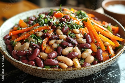 Colorful mixed bean salad with carrots, bell peppers, and fresh herbs in a rustic bowl on a marble table