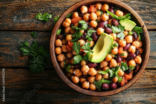 Chickpea and kidney bean salad with avocado and fresh parsley in wooden bowl on rustic table, healthy plantbased meal idea