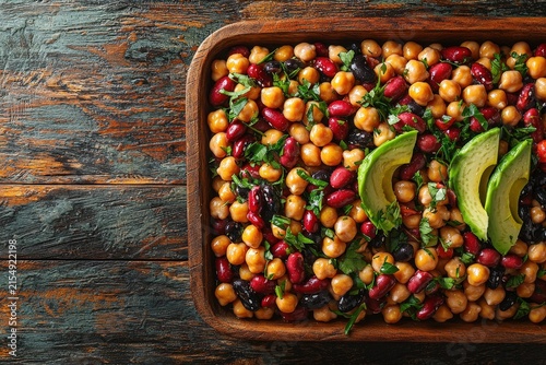Colorful chickpea kidney bean avocado salad with herbs in wooden bowl on rustic table, healthy vegan protein meal