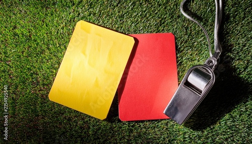 vibrant yellow and red penalty cards resting beside a metal referee whistle on the green grass of a soccer field
