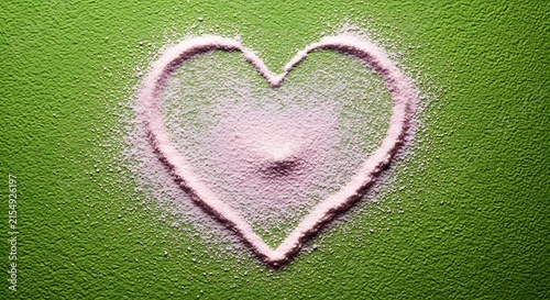 Pink heart shape made of salt on green textured background, symbol of love and health