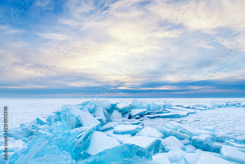 Ice floes with snow on Baikal lake in winter. Blue sky with clouds at sunrise. Olkhon island, Baikal, Siberia, Russia.