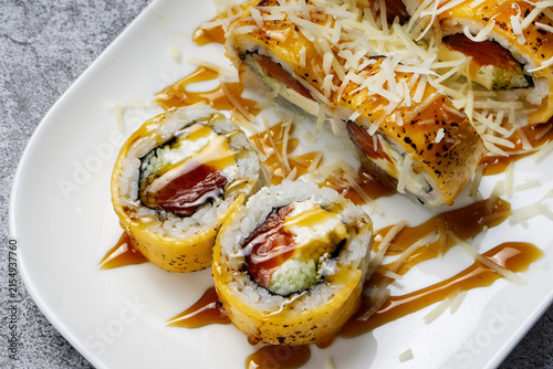 A cheese sushi roll on a plate, topped with sauce and sprinkled with Parmesan.