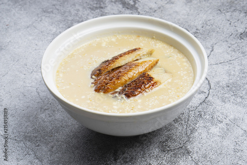 Traditional Asian miso soup topped with grilled unagi eel fish against grey concrete background. Creamy fish soup with smoked eel in a white bowl, side view close up with copy space.