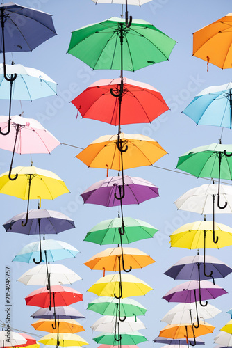 Картината върху платно Low angle view of numerous colorful hanging umbrellas floating against a clear b