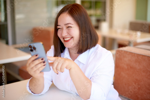 laughing woman using smartphone sitting in cafe terrace