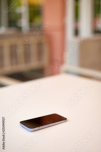 smartphone lying on white table with dark blank screen on blurred cafe terrace background
