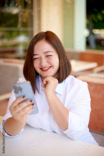 joyful woman using smartphone and waiting cappuccino at outdoor restaurant