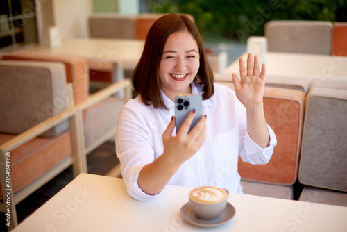 smiling woman having online video chat on mobile phone at coffee shop terrace