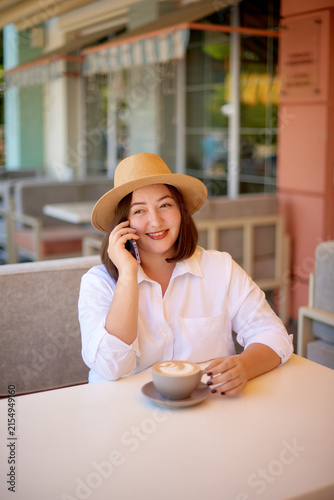 woman in hat talking and relaxing coffee break with fresh latte at street cafe terrace