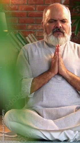 Indian senior man sitting peacefully on the floor in traditional kurta pyjama, practicing deep breathing, yoga, or meditation at his modern home
