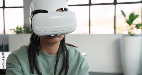 Non-binary African adult in office chair wearing white VR headset, rotating tablet, testing VR app