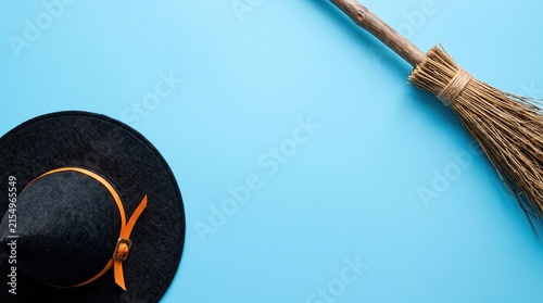 A black witch hat and a rustic wooden broomstick isolated on a bright light blue background for halloween celebration