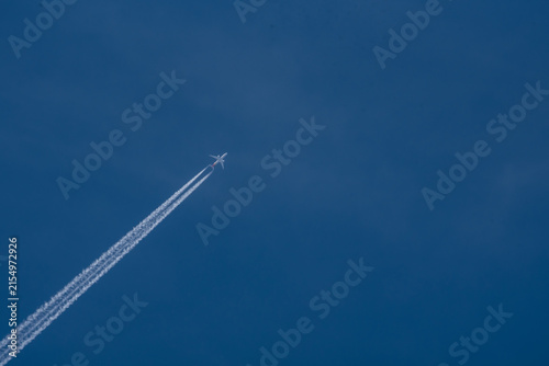 Commercial airplane flying high in the clear blue sky leaving a long white contrail vacation travel holiday