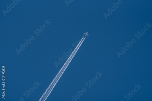 Commercial airplane flying high in the clear blue sky leaving a long white contrail vacation travel holiday