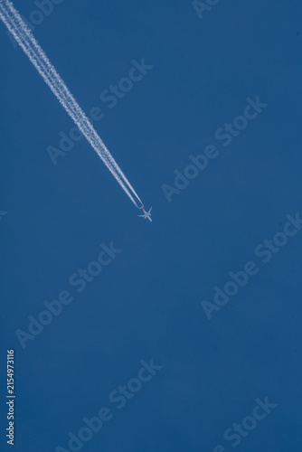 Commercial airplane flying high in the clear blue sky leaving a long white contrail vacation travel holiday